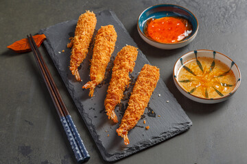 Tempura de crevettes sur une ardoise avec des sauces et baguettes sur un fond noir. Cuisine japonaise.