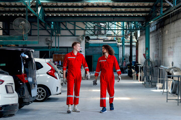 Two handsome mechanic men in red uniform walking through row of vehicle at garage, auto mechanic technician friend work together to repair and maintenance customer car automobile at car service shop.