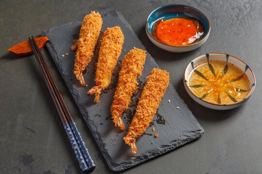 Tempura de crevettes sur une ardoise avec des sauces et baguettes sur un fond noir. Cuisine japonaise.