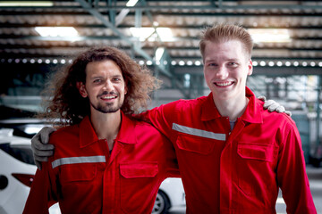 Two mechanic men in red uniform hugging and walking through row of vehicle at garage, auto mechanic technician friend work together to repair and maintenance customer car automobile at service shop.