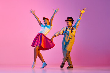 Emotional and stylish children, boy and girl in retro clothes dancing lindy hop against pink studio background in neon light. Concept of childhood, hobby, active lifestyle, performance, art, fashion