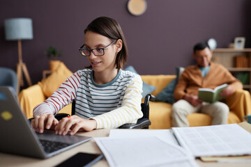 Portrait of smiling teenage girl with disability using computer at home while studying online, copy...