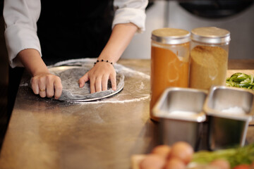 Restaurant cook flattening and shaping dough on pizza tray