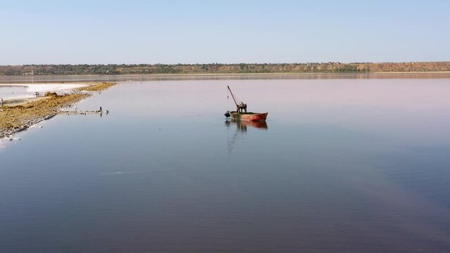 Small fishing boat with men sailing at sea firth. Three fishermen pulling out thier catch. Peloid production, Kuyalnik.