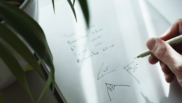 Close up shot of a hand trying to solve a geometry problem by drawing 90 degree angle in a notebook at daytime.