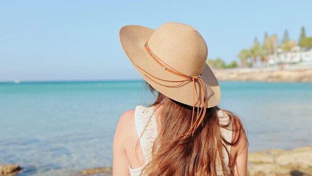 Attractive young Caucasian woman at the beach, sunbathing during summer vacation. Girl enjoys a relaxing trip by the sea. Beautiful happy joyful lady wearing hat. Travelling concept.