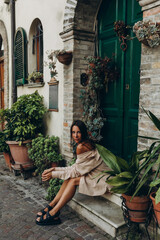 A young girl in an Italian courtyard sits on the threshold against the background of a green door...