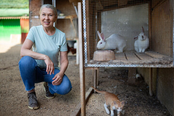 A farmer woman next to a cage with a white rabbit.