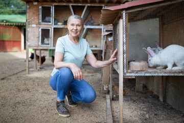 A farmer woman next to a cage with a white rabbit.