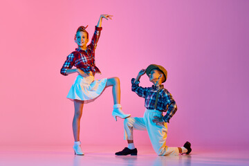 Children in stylish retro clothes making performance, dancing against pink studio background in...