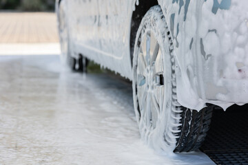 Aesthetic photo of a gray hatchback covered with dirt foam at an open car wash. Dripping stump from...