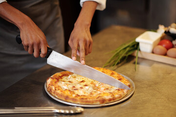 Chef cutting hot freshly baked pizza into slices