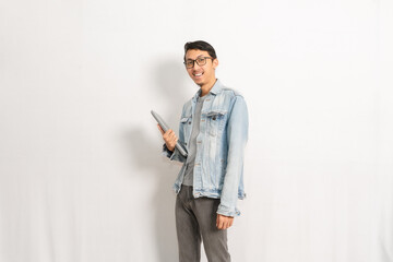 A confident male holding his laptop while looking to the camera. Indonesian or southeast asian model isolated with white wall background.