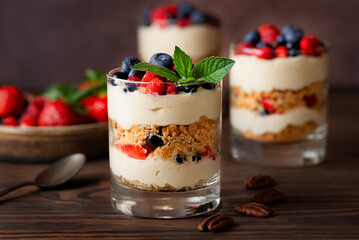 Sweet dessert in a glasses with berries, mint, whipped coconut cream and biscuit on a wooden table. Healthy food, vegan, sugar, gluten and lactose free.