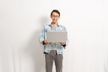 A confident male model gives happy expression when he looking to his laptop. Indonesian or southeast asian model isolated with white wall background.
