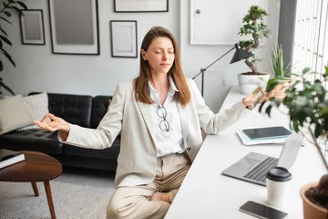  Office zen. Calm european businesswoman meditating with closed eyes in lotus position, feeling peaceful and balanced © Prostock-studio