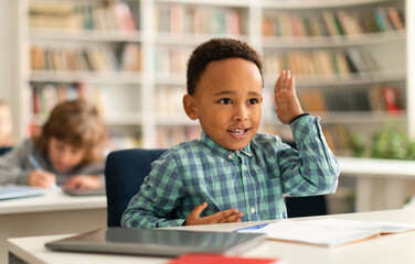 Smart black boy raising his hand to answer a question during lesson in elementary school, kid engaging in the lesson