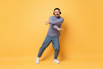 Fototapeta na wymiar Carefree Young Asian Guy Wearing Wireless Headphones Dancing On Yellow Background