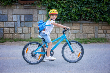Cute child, boy with helmet and backpack, riding bike at the evening in rural nature