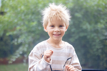 Cute little boy with static electricy hair, having his funny portrait taken outdoors on trampoline
