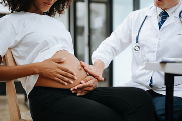 Obraz premium Pregnant african woman has appointment with doctor at clinic. Male gynaecologist OB GYN medic specialist with stethoscope listens to baby's heartbeat in mother's belly. Pregnancy, health care