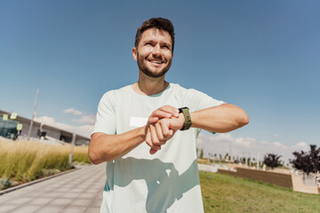 A confident male athlete trainer uses a fitness watch for cardio measurement in the app, training outside in sportswear. Healthy lifestyle and mental health.