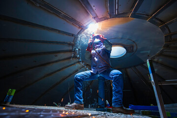 Welding male worker metal arc is part roof tank dome inside confined spaces.