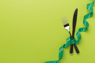 Knife and fork wrapped in tape measure on color background, top view