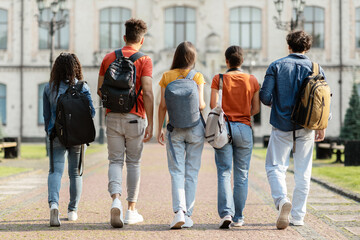 Group of five students with backpacks walking at university campus together