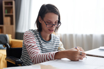Side view portrait of young girl with disability wearing glasses and doing homework while studying from home, copy space