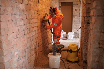 Construction worker grinding brick  wall using grinding machine with vacuum cleaner attached to...