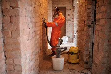 Construction worker grinding brick  wall using grinding machine with vacuum cleaner attached. No...