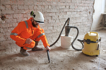 Male constriction site worker cleaning concrete floor from dust with vacuum cleaner after...