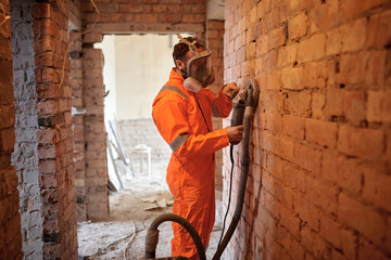 Construction worker cleaning brick  wall using grinding machine with vacuum cleaner attached.