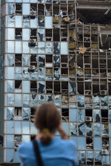 unrecognizable girl back to camera stands in front of building destroyed by unmanned aerial vehicle