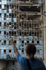 unrecognizable girl back to camera points at building destroyed by unmanned aerial vehicle. Civil infrastructure damaged by war drones. Selective focus