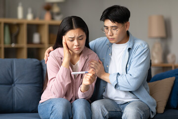 Depressed Korean Couple Holding Negative Pregnancy Test Sitting At Home