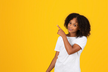 Glad cheerful adolescent african american girl in white t-shirt, point finger to empty space
