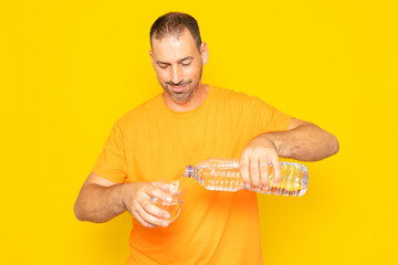 Hispanic man with a beard in his 40s pouring water into a glass, salable habit. Isolated on yellow...