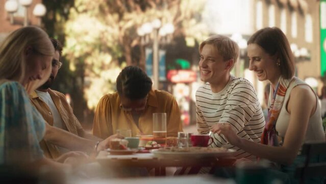 Multiracial Group of Friends Enjoying Leisure Time in a Street Cafe. Young Women and Men Having Fun Conversations Behind a Table, Enjoying Tasty Food and Beverages. African Girl Sharing Stories
