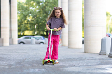 Preschooler little girl riding a scooter in city. Active leisure and outdoor sport for child and kid on summer day. urban transport for kid