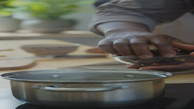 Vertical close up shot of hands of unrecognizable African American man adding dried hibiscus leaves and spices into pot with boiling water while preparing Zobo tea at home