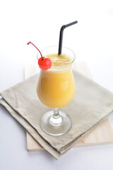 cold iced summer orange mango fruit juice with red cherry in cocktail glass black straw on grey cloth white background asian beverage halal food drink menu for hotel bar cafe