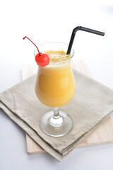 cold iced summer orange mango fruit juice with red cherry in cocktail glass black straw on grey cloth white background asian beverage halal food drink menu for hotel bar cafe