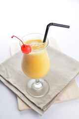 cold iced summer orange mango fruit juice with red cherry in cocktail glass black straw on grey cloth white background asian beverage halal food drink menu for hotel bar cafe
