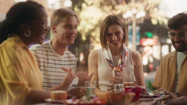 Group of Young Diverse Friends Having Fun, Talking, Laughing and Telling Jokes. Beautiful Multiethnic Men and Women Sitting Behind a Table, Socializing on a Summer Terrace of a Restaurant