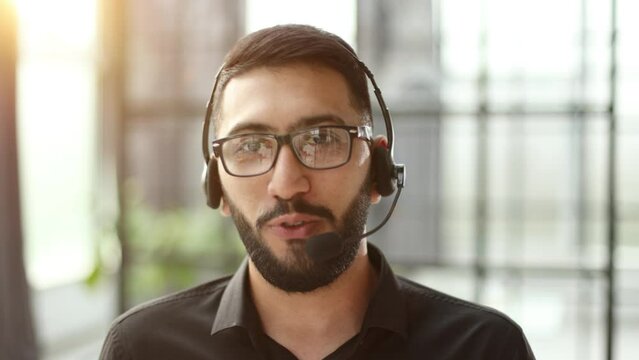 Focused businessman telemarketer telesales agent wear wireless headset make conference video call talk consult online client on computer, male helpline operator work in customer care support office