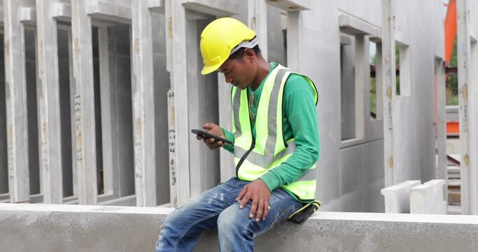 Happy worker enjoying free time and using smartphone. Asian man forman warehouse worker sitting on workshop site break relax time at Heavy Industry Manufacturing Prefabricated concrete walls Factory