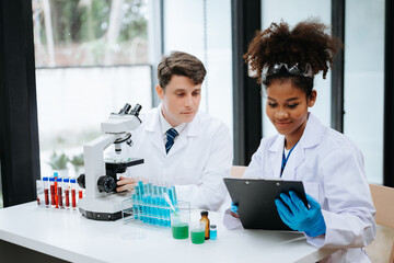Focused mature male doctor and African female nurse look at tablet and laptop screen discuss anamnesis together. Concentrated diverse medical professionals