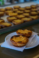 Two traditional Portuguese pasteis de nata on plate with pasteis in showcase on background.